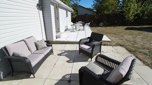 A patio area with wicker furniture and a white building in the background. - Plovers Cove Cottage (Wasaga Beach)