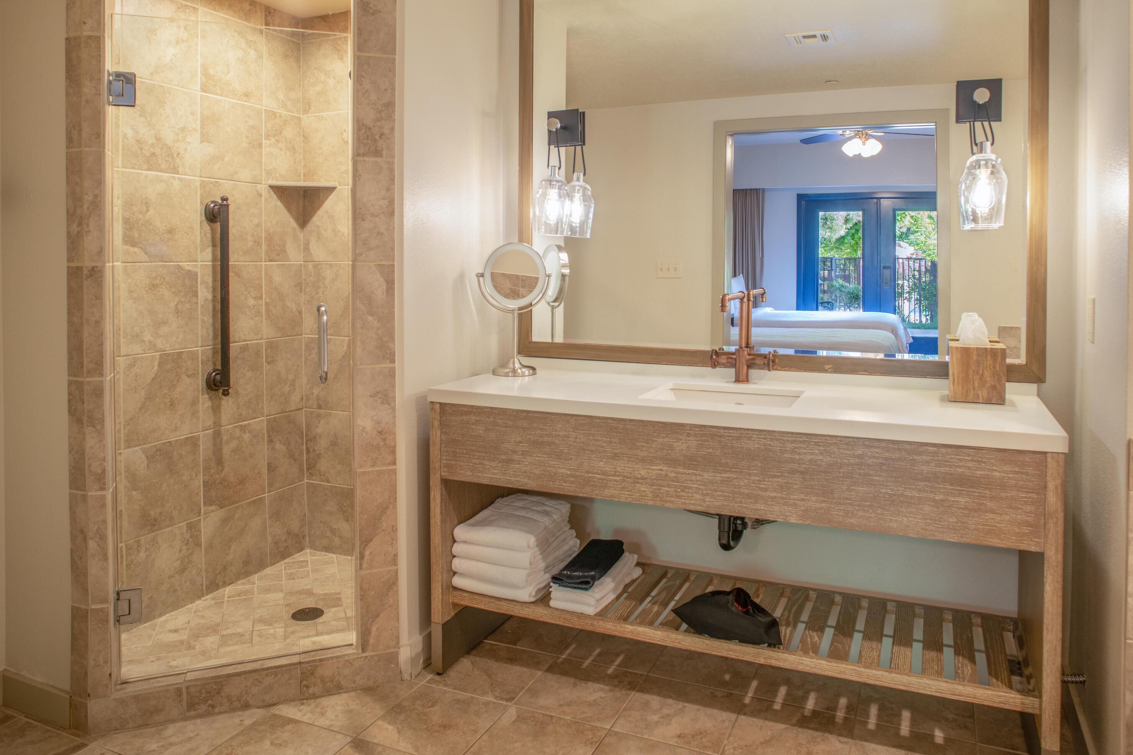 Une salle de bain moderne équipée d’une douche, d’un meuble-lavabo avec miroir et d’un porte-serviettes.