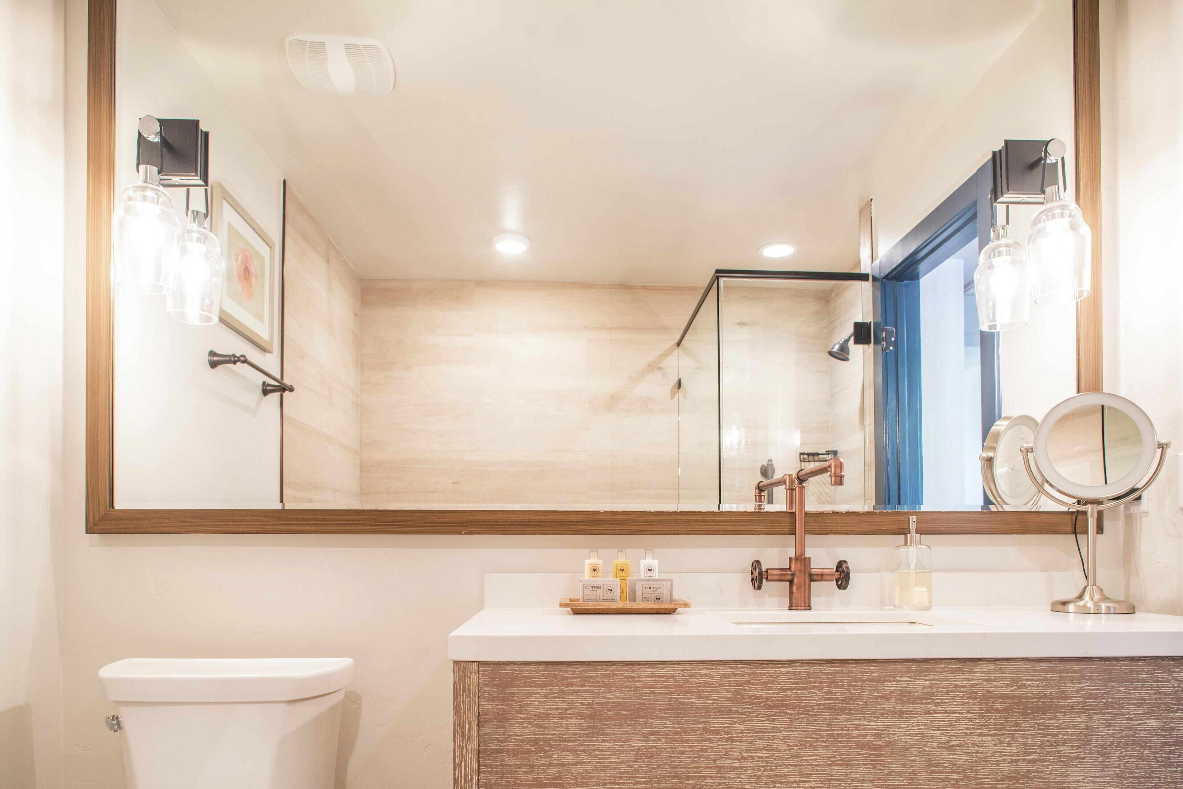 Een moderne badkamer met een grote spiegel, een wastafel met een houten kastje en een toilet.