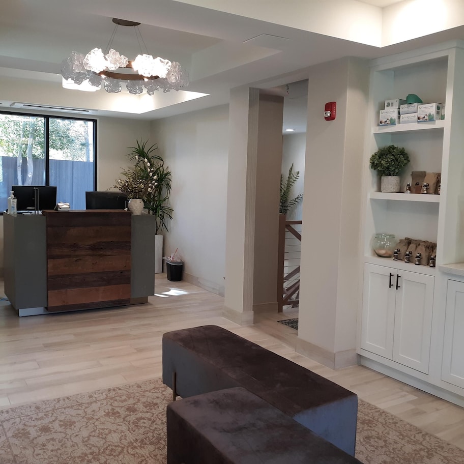 A reception area with a wooden reception desk, a bench, a potted plant, and a shelf with toiletries.