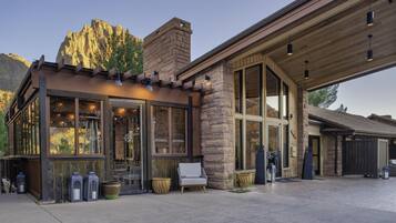A modern building with large windows, stone walls, and a covered outdoor area with seating.