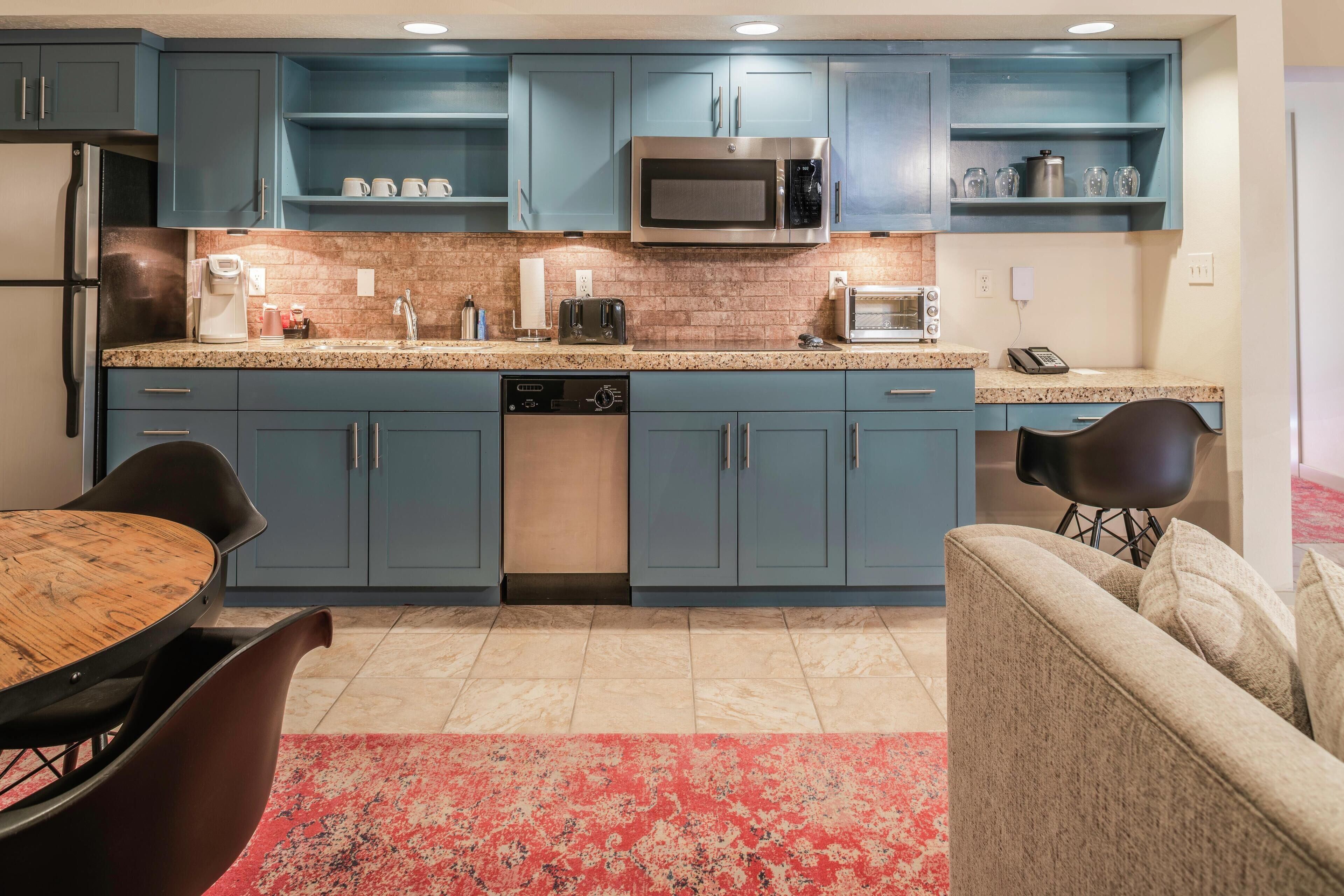 A modern kitchen with blue cabinets, stainless steel appliances, a granite countertop, and a dining area with a wooden table and chairs.