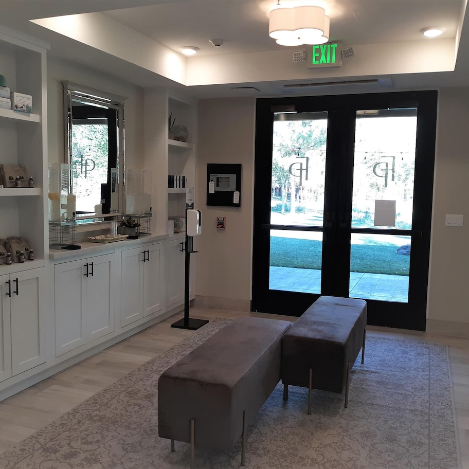 A modern kitchen with white cabinets, a countertop with various items, a bench, and a large window with a view of the outdoors.