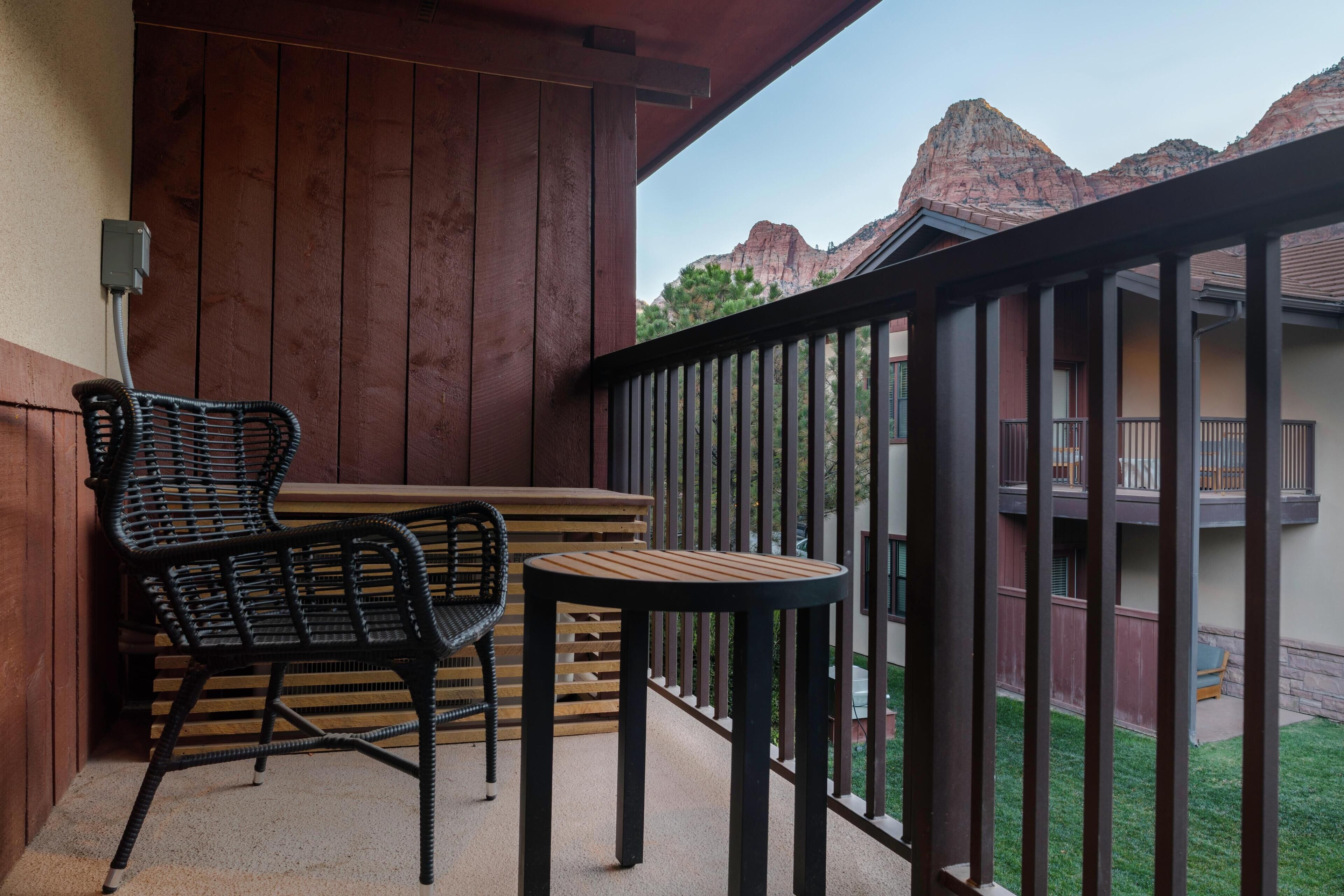 Ein Balkon mit zwei Korbstühlen und einem Holztisch, mit Blick auf eine Berglandschaft.