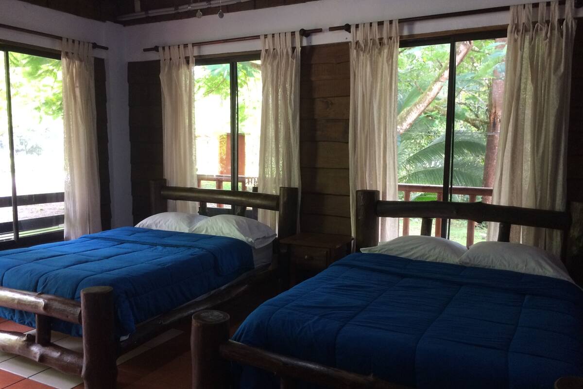 Two wooden beds with blue bedding, a wooden headboard, and a window with curtains.