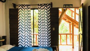 A bedroom with a bed, a nightstand, and a window with chevron-patterned curtains. - Hotel Samsara (Bahía Ballena)