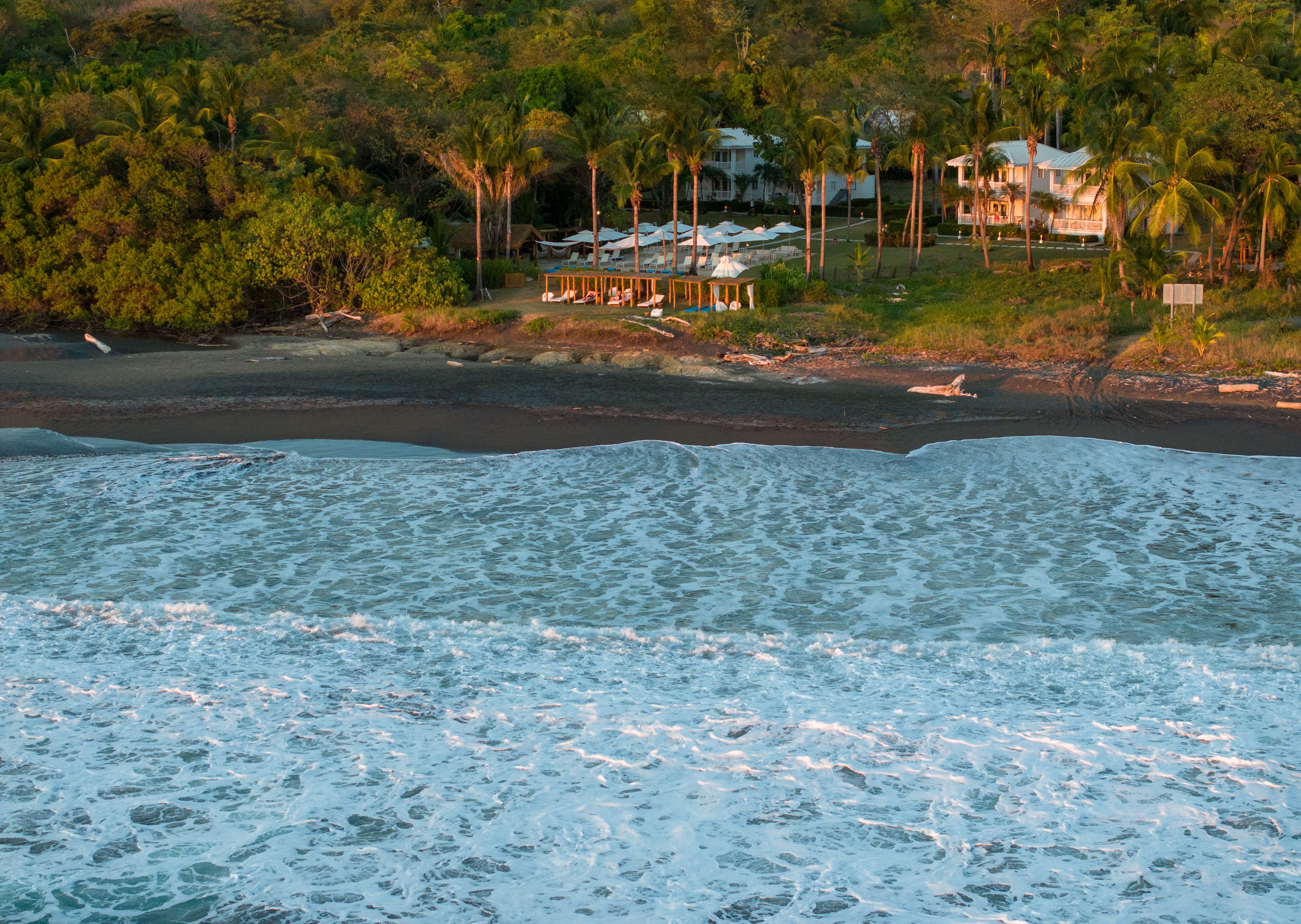 A beach with a house and lounge chairs in the background.