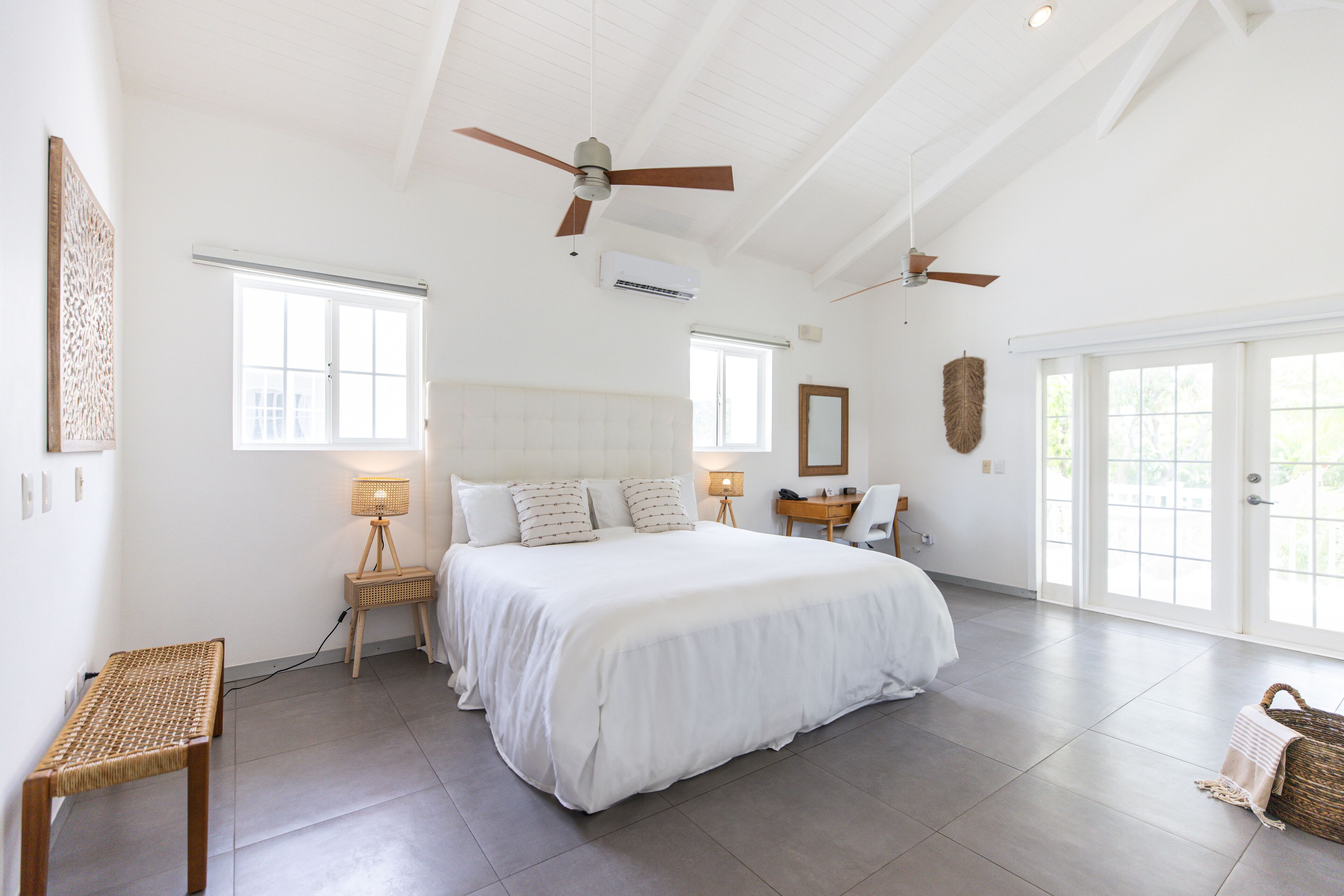 A spacious bedroom with a large bed, two ceiling fans, a bedside table with a lamp, a chair, and a large window.