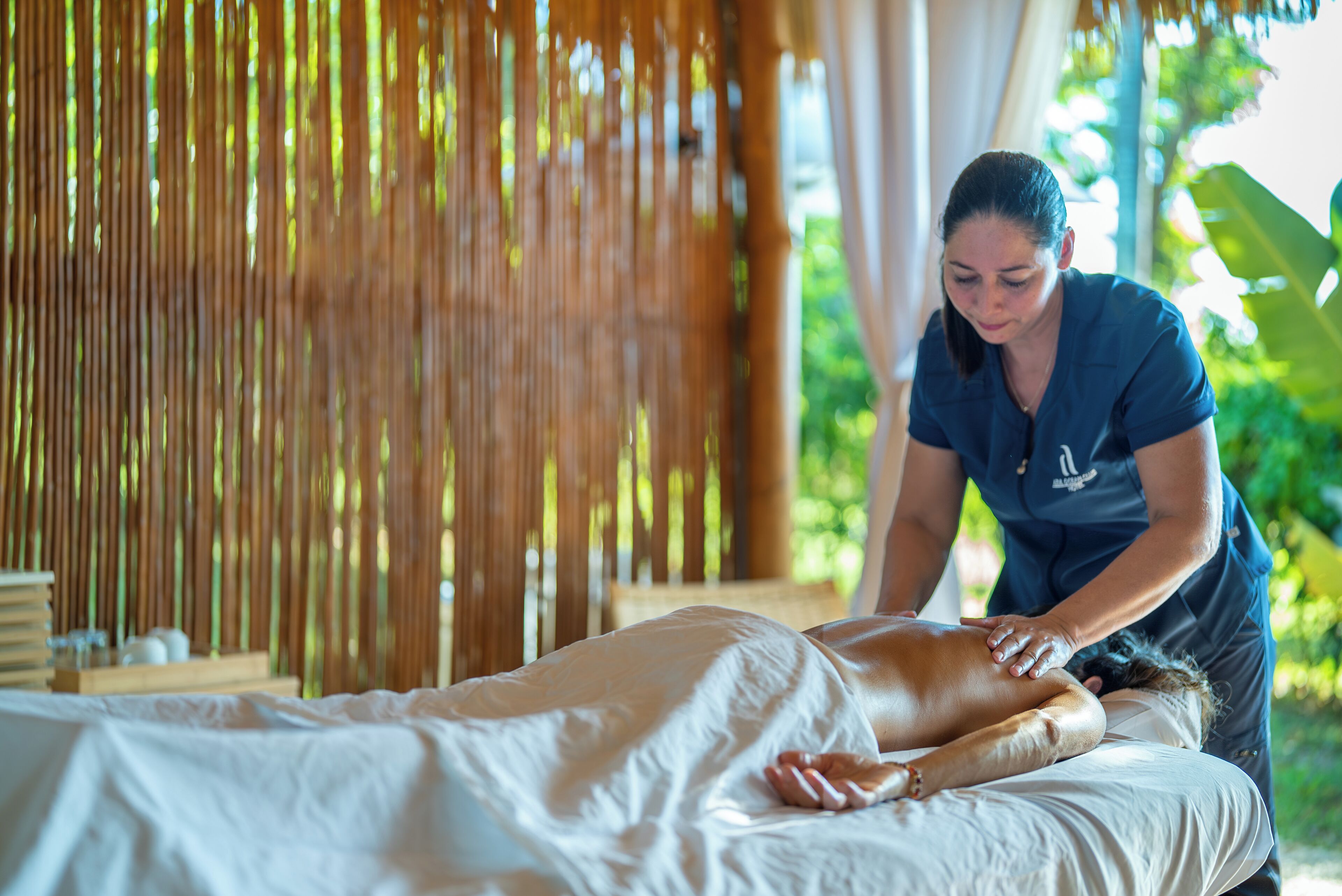 Een massagesessie in een ruimte met een bamboeachtergrond en een bed met een wit laken.