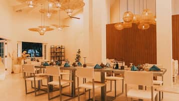 Àmplia zona de dinar amb diverses taules i cadires, amb lluminàries penjants úniques i una paret decorativa de fusta.