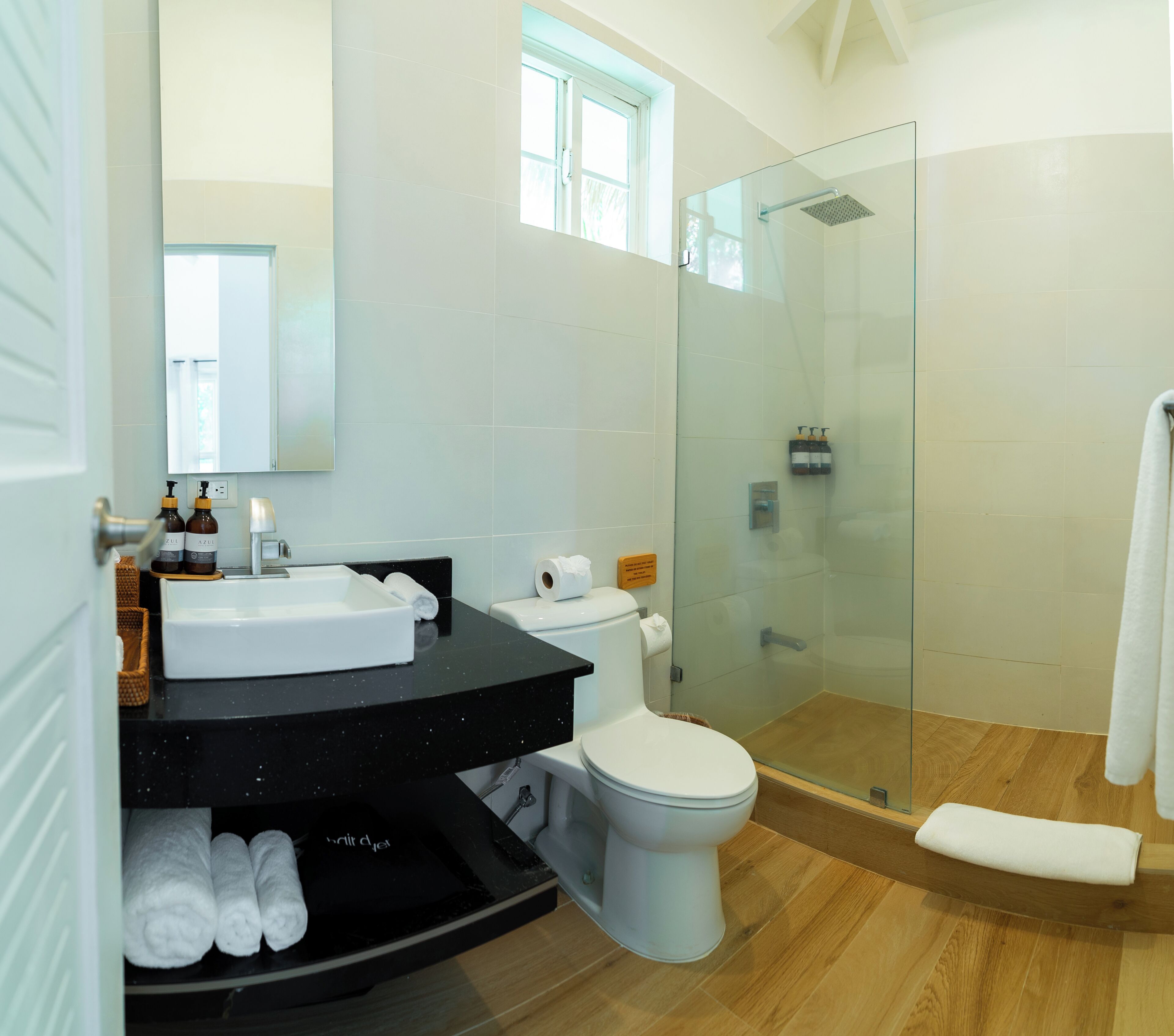 Un baño moderno con ducha de vidrio, inodoro blanco y tocador negro con espejo.
