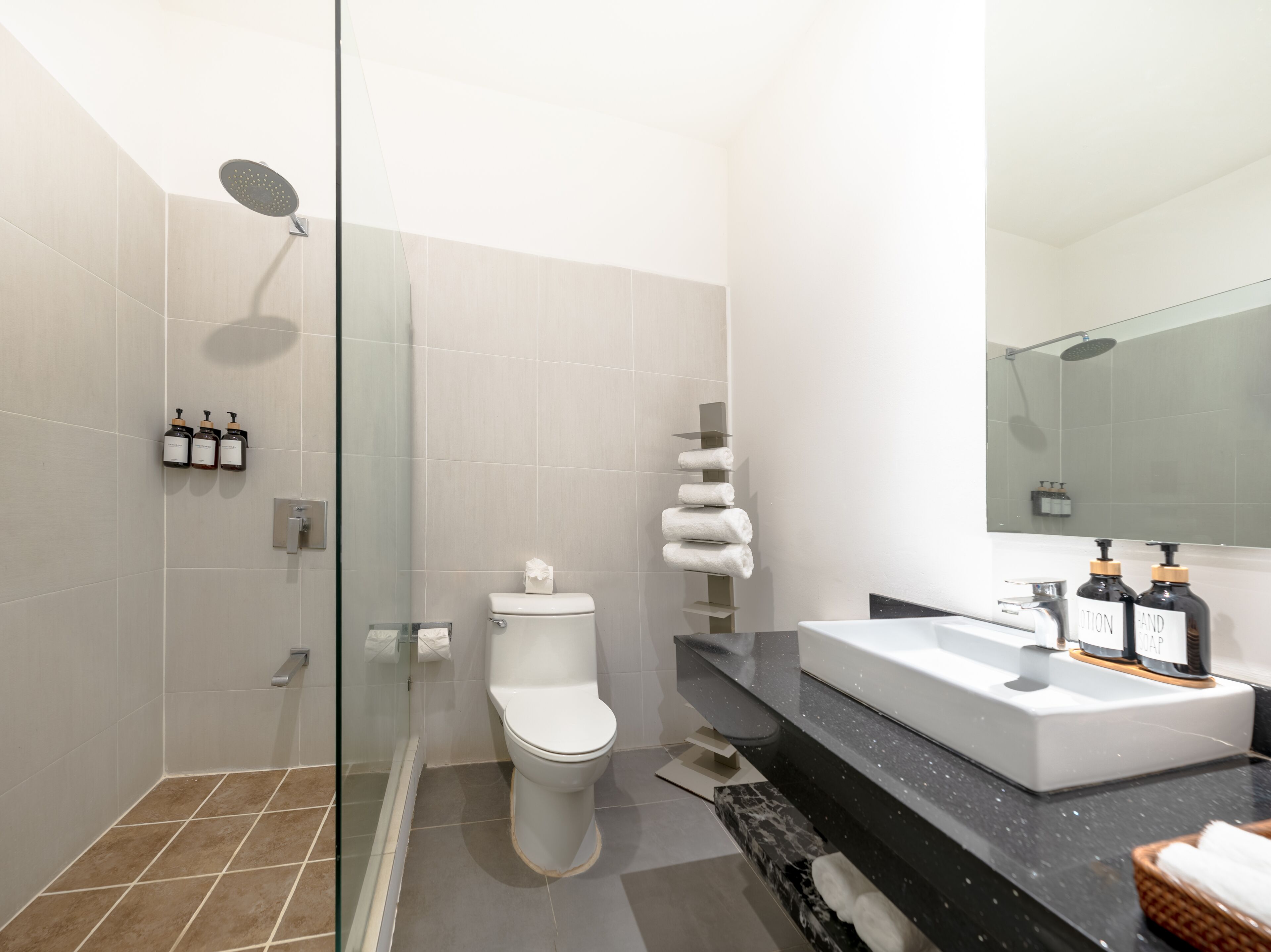 A modern bathroom with a glass-enclosed shower, a toilet, a sink with toiletries, and a mirror.