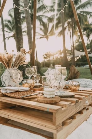 A wooden table set outdoors with glassware and decorative items, surrounded by palm trees. - Azul Hotel & Retreat  (Cuajiniquil)