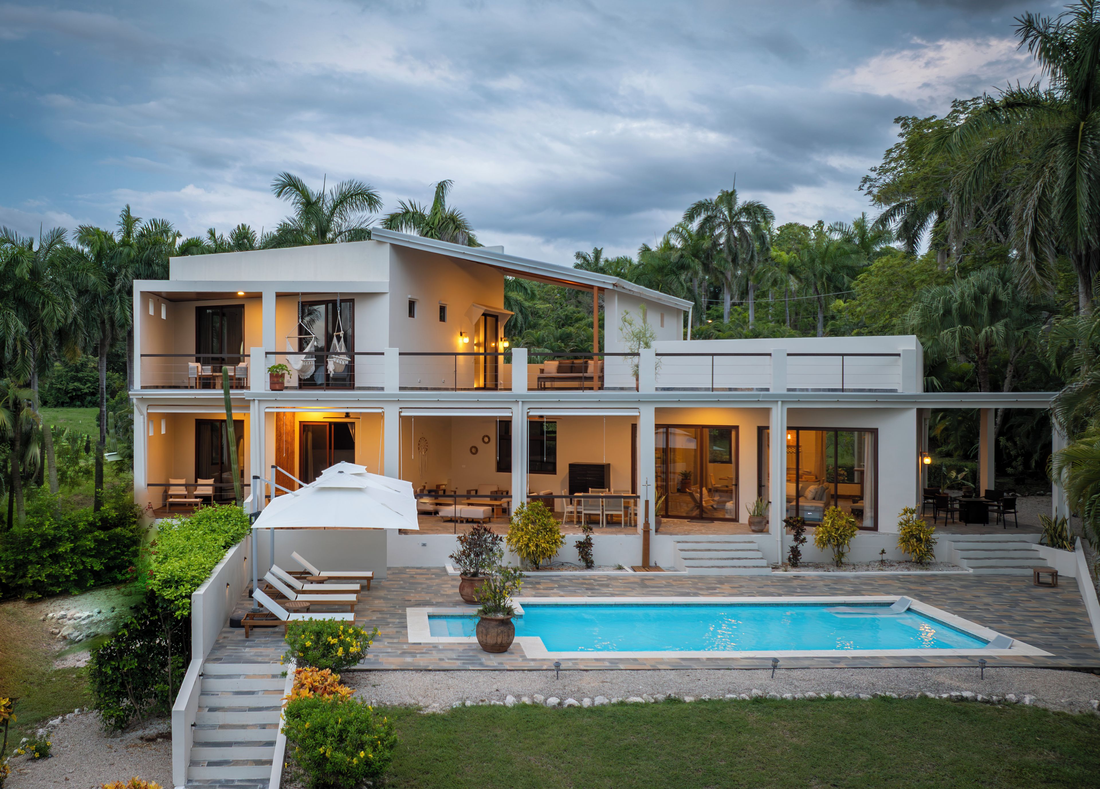 A two-story modern house with a swimming pool, outdoor seating, and a garden.