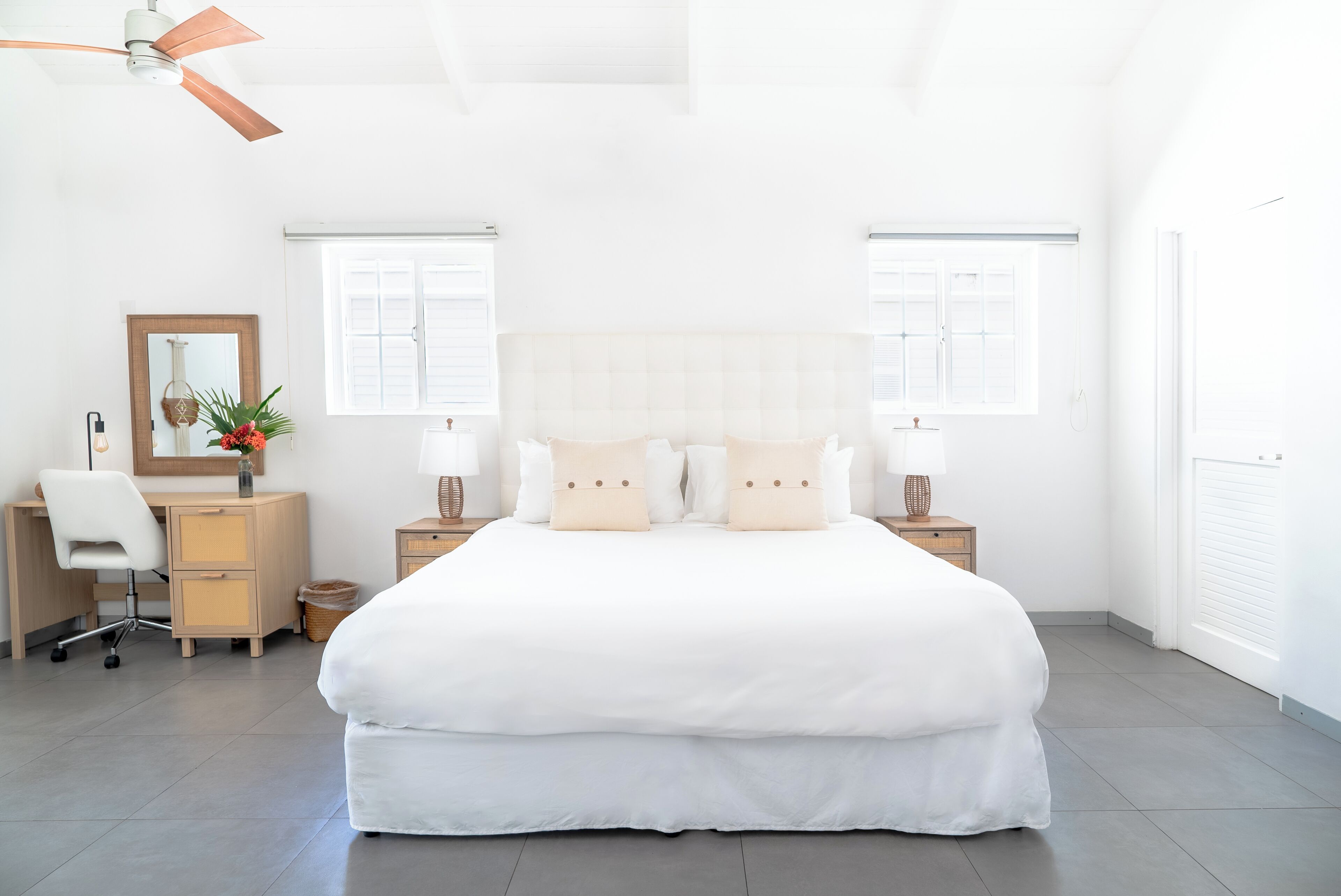 A modern bedroom with a large bed, a desk, a chair, and a ceiling fan.