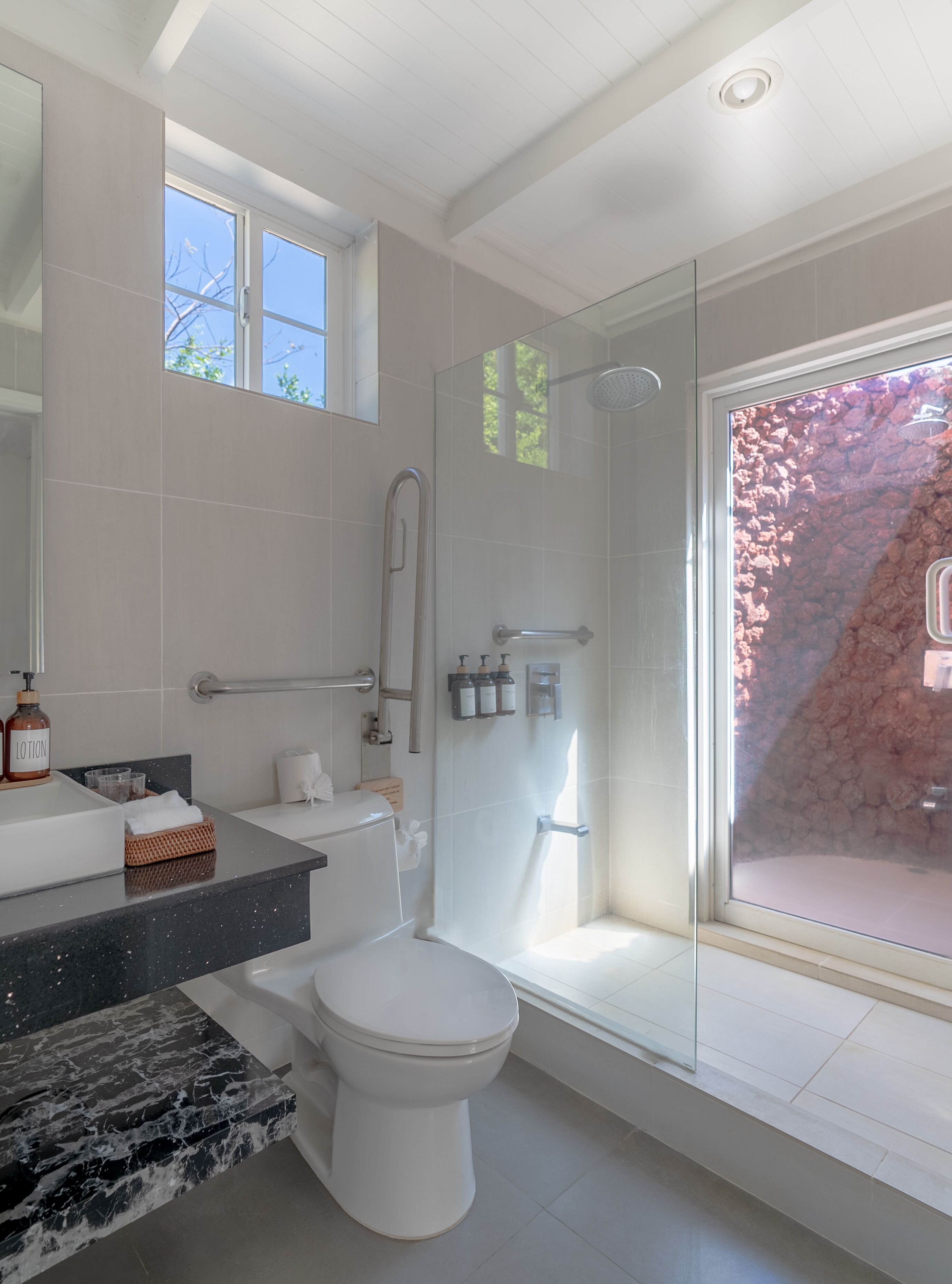 A modern bathroom with a glass shower enclosure, a marble countertop, and a toilet.