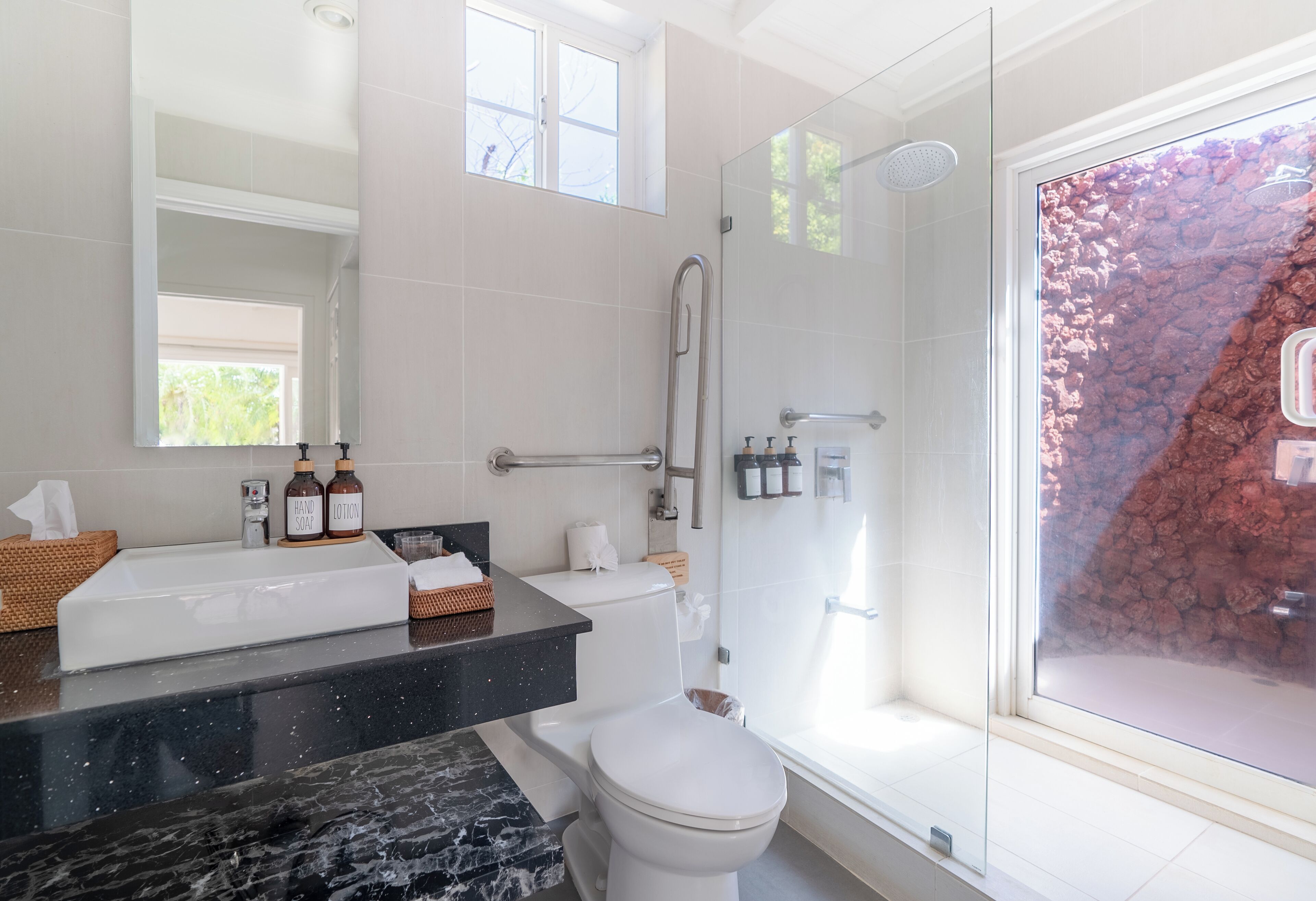 A modern bathroom with a glass shower enclosure, a white toilet, and a black marble sink.