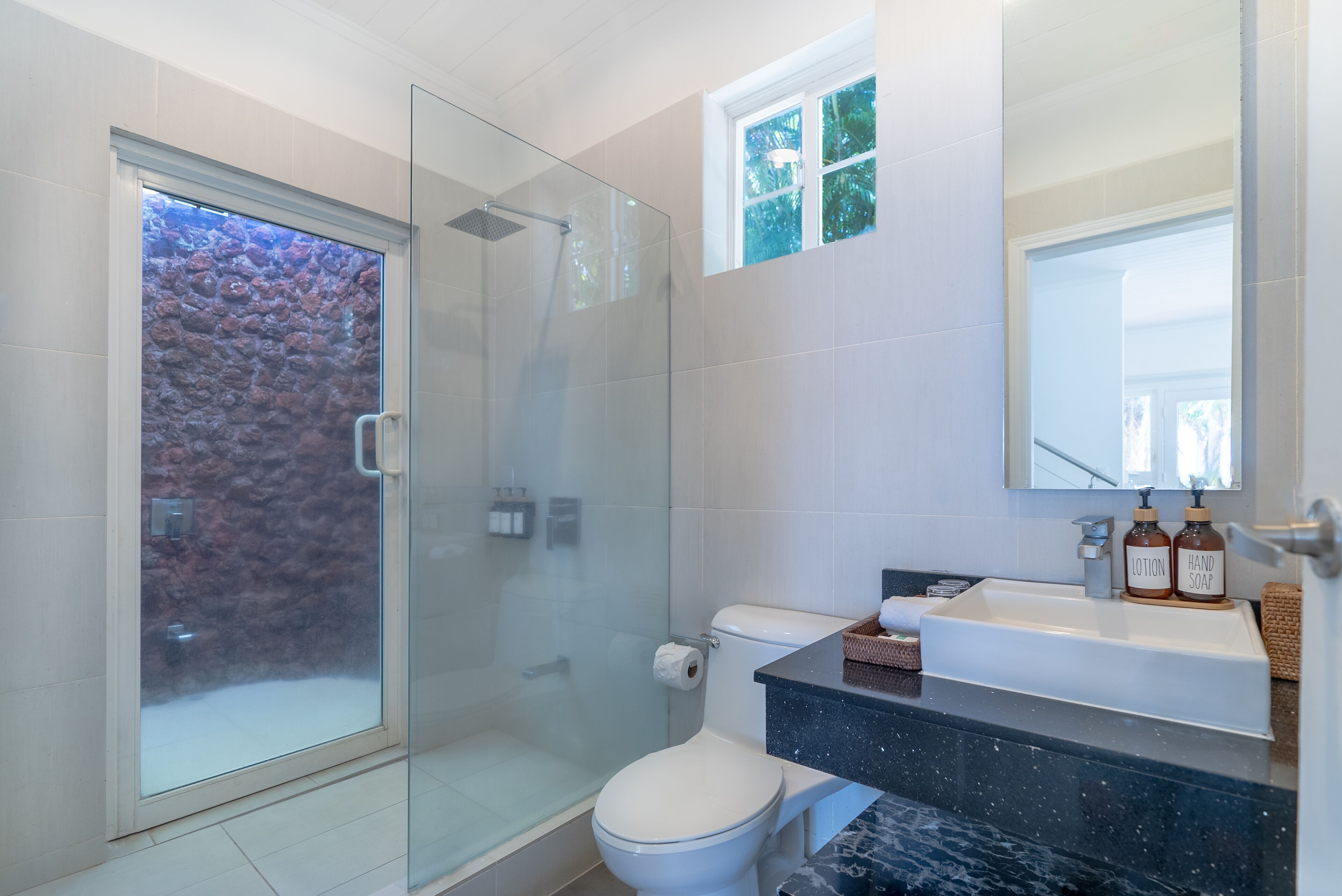 Une salle de bain moderne avec une douche à parois de verre, des toilettes blanches, un lavabo en marbre noir et un miroir au-dessus du lavabo.