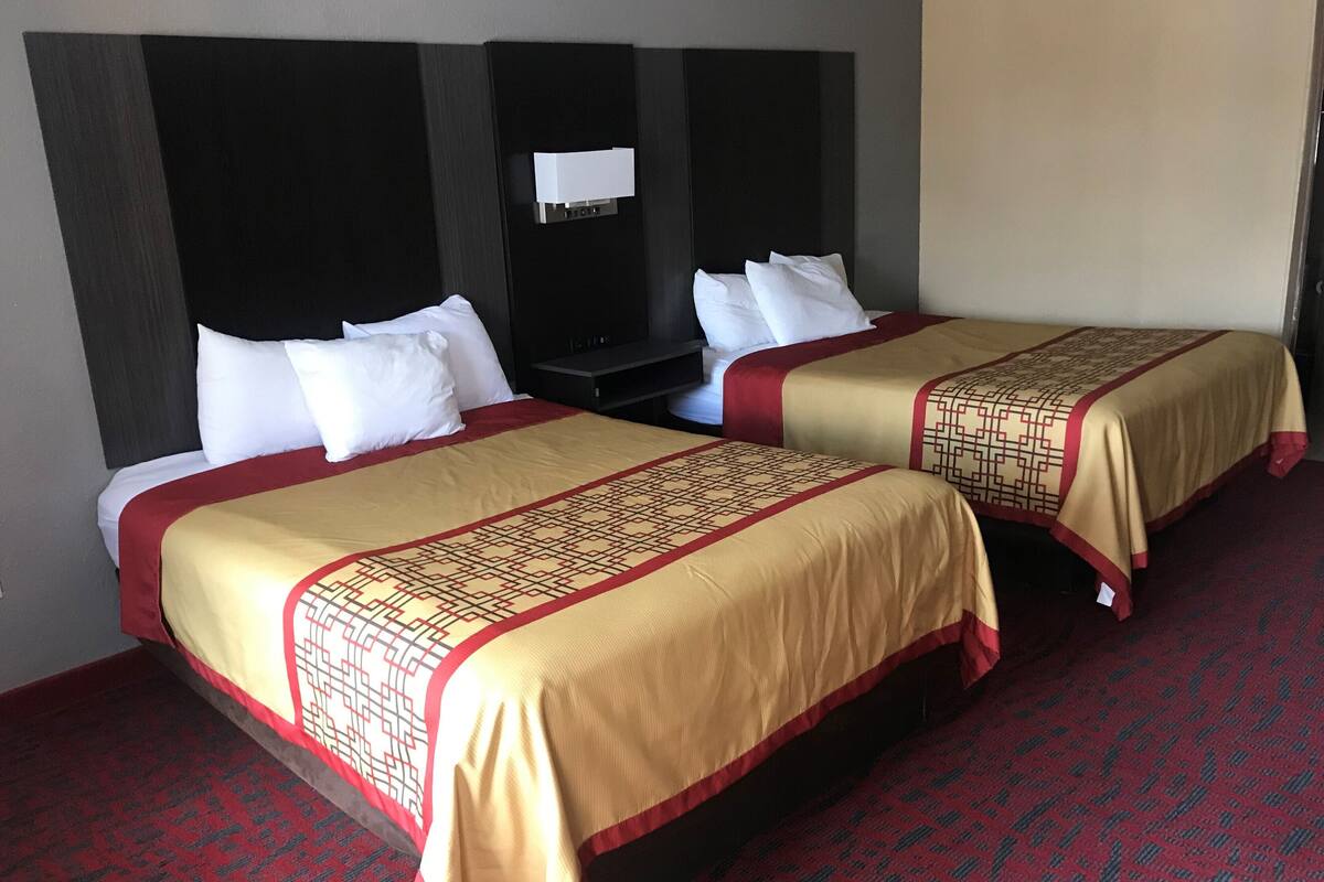 Two double beds with red and beige bedding, a dark headboard, and a red carpeted floor.