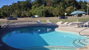 A swimming pool with a curved design, surrounded by a metal fence and equipped with a ladder. - Conner Hill Motor Lodge (Pigeon Forge)