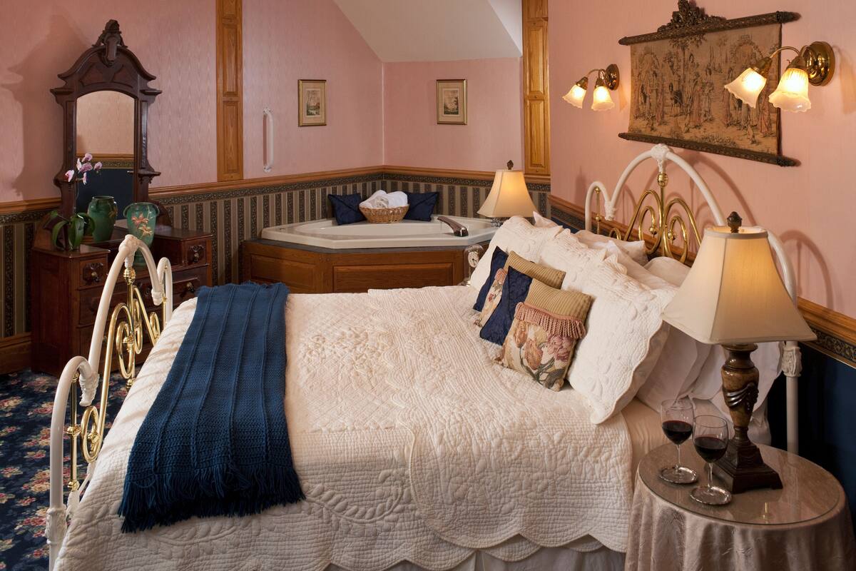 A bedroom with a large bed, a nightstand with a lamp, a dresser, and a mirror.
