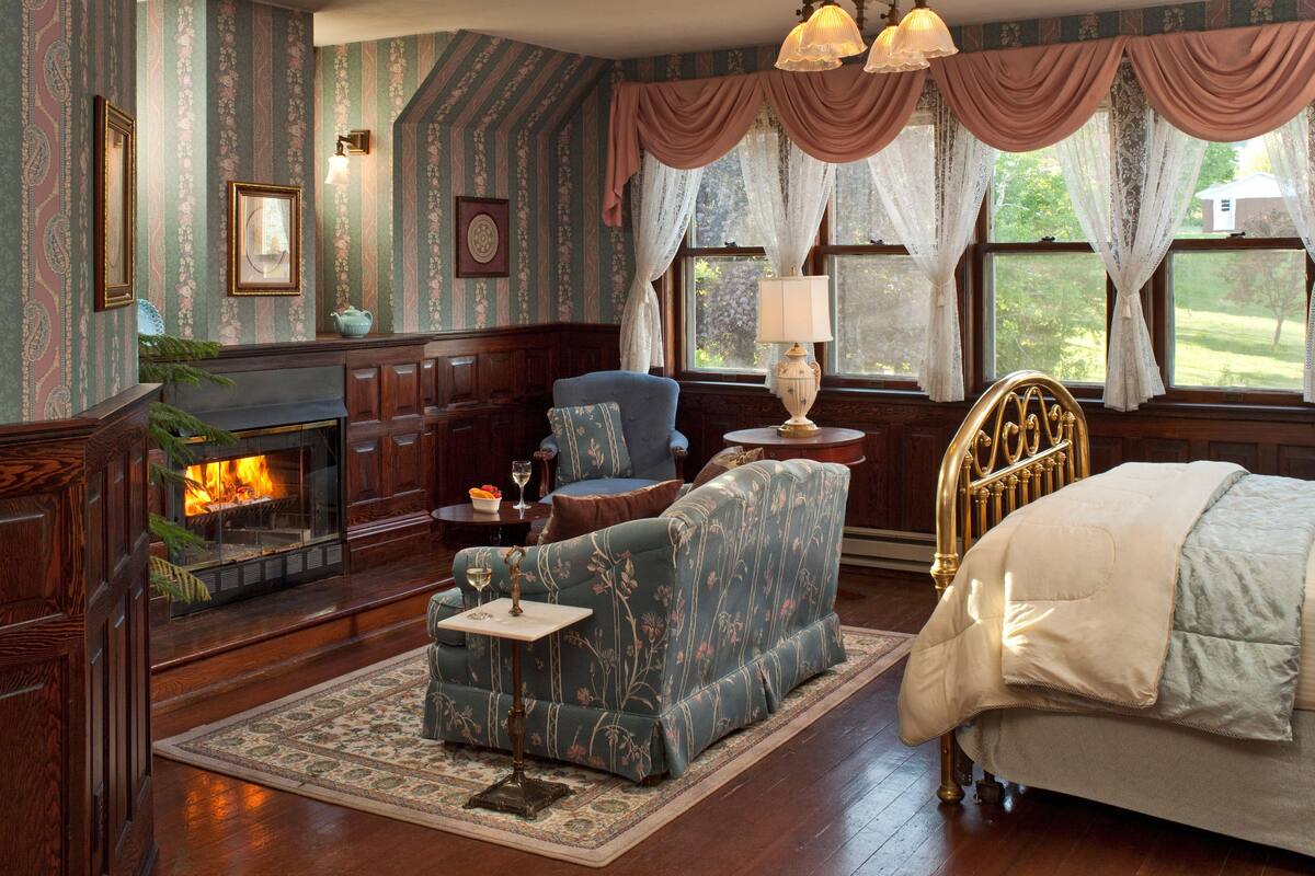 A cozy room with a fireplace, a sofa, a bed, and a nightstand with a lamp.