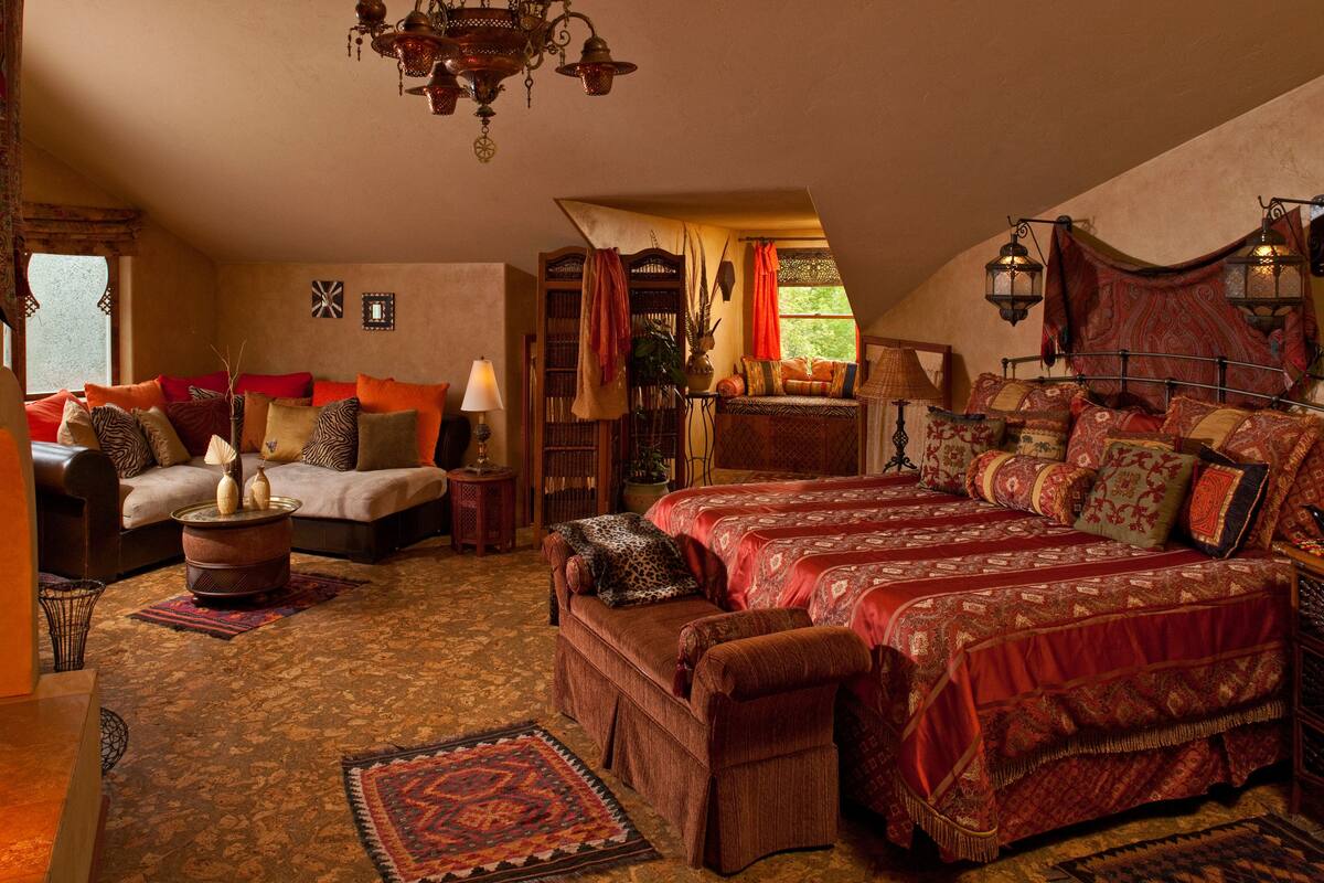 A traditional room with a sofa, a bed with patterned bedding, a small table with a lamp, and a decorative ceiling light.