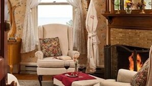 Uma sala de estar acolhedora com lareira, uma poltrona confortável e vista para o mar pela janela.