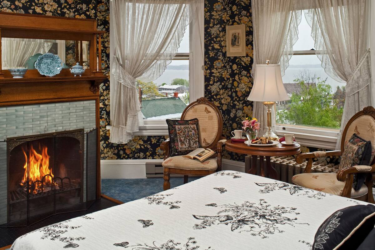 A cozy room with a fireplace, floral wallpaper, and a view of the outdoors.