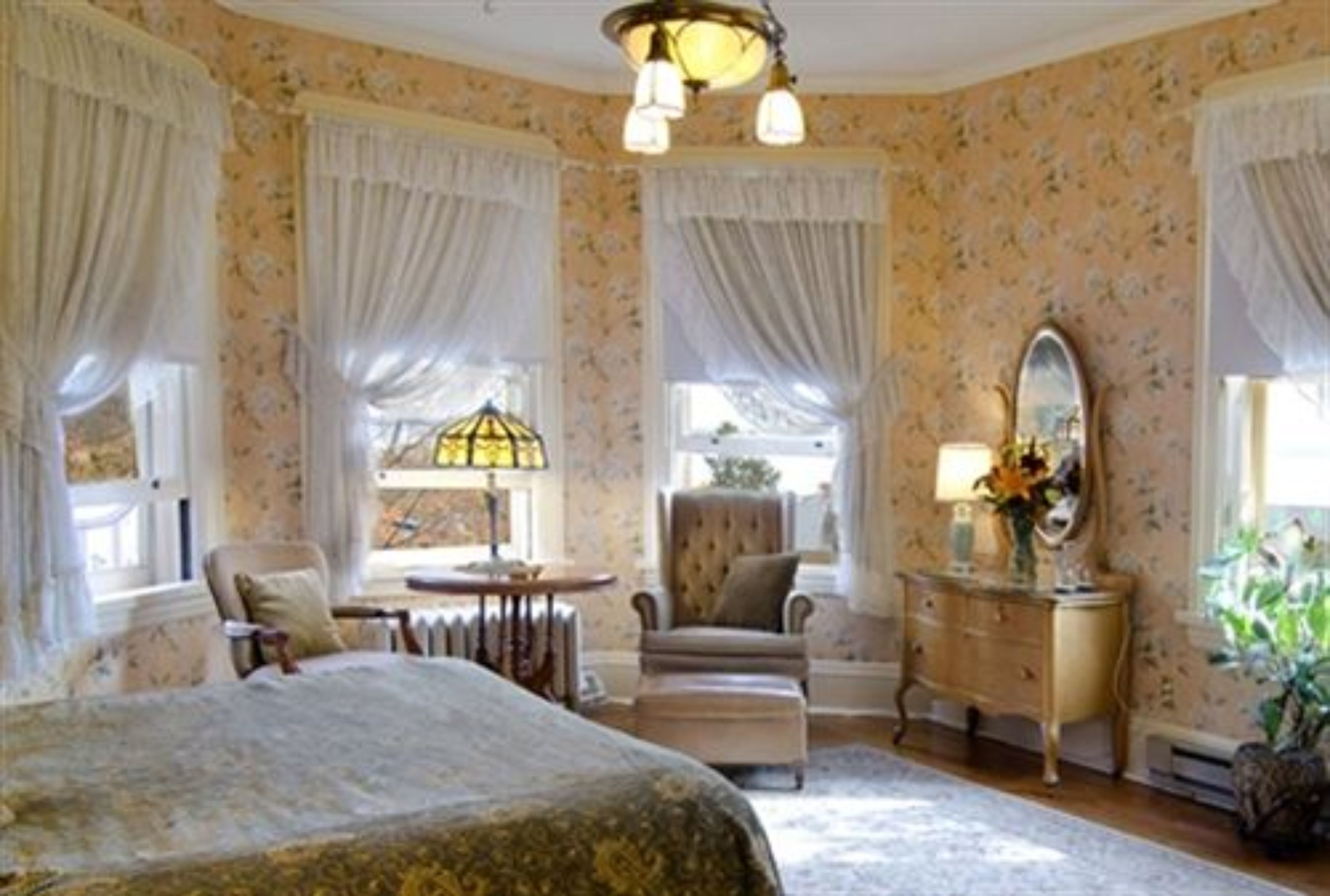 A classic bedroom with a large bed, a dresser, a chair, and a table.