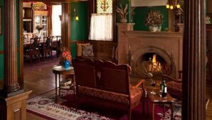 Quarto tradicional com lareira, um sofá e um espaço de jantar visível ao fundo.