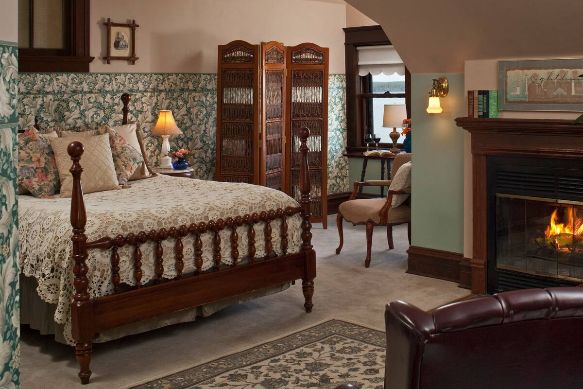 A bedroom with a four-poster bed, a fireplace, and a chair.