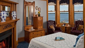 Quarto com lareira, mobiliário de madeira, cama com um livro e vista para a água.