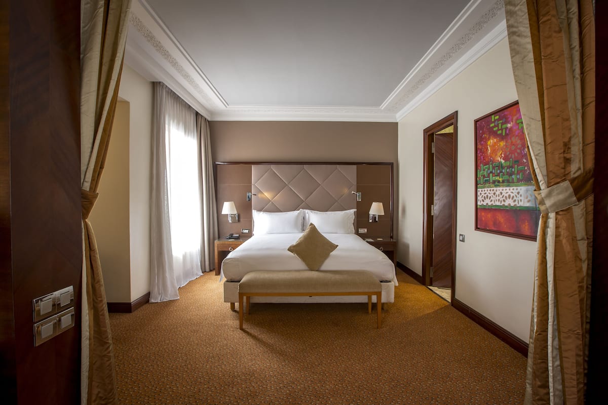 Habitación de hotel con una cama grande, mesitas de noche con lámparas, un banco y un cuadro en la pared.