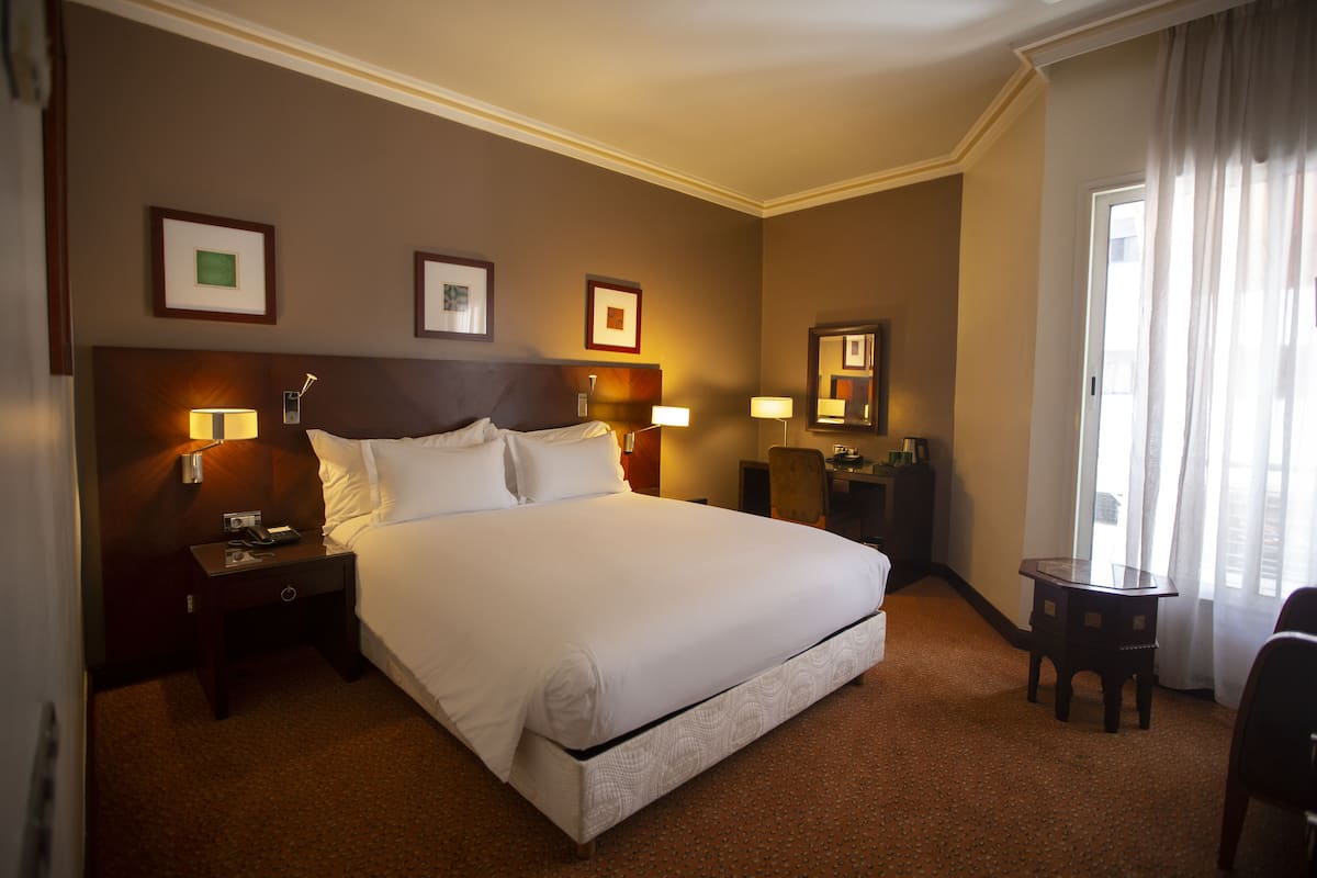 Una habitación de hotel con una cama grande, dos mesitas de noche, una mesa pequeña y un espejo.