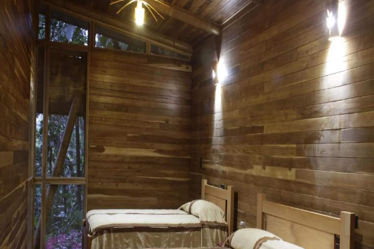 A wooden cabin room with two beds, a wooden ceiling, and a window.