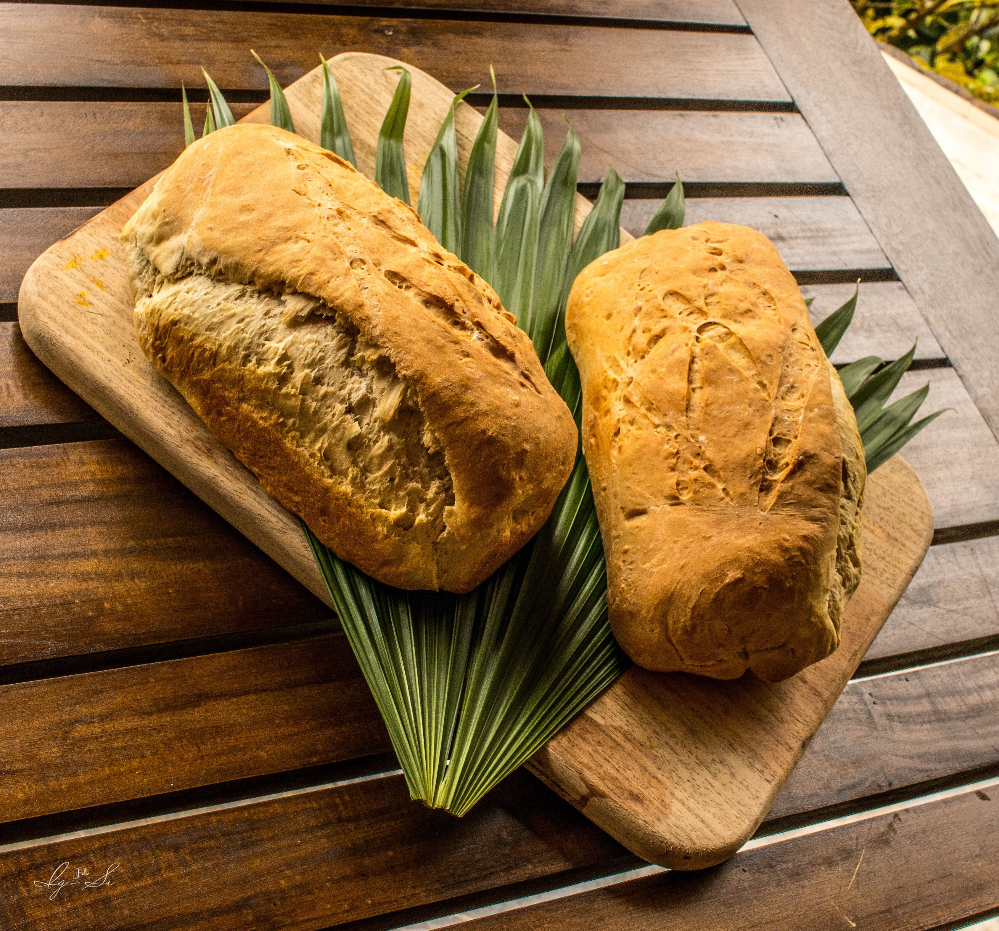 Två limpor bröd på en träskärbräda med gröna blad.