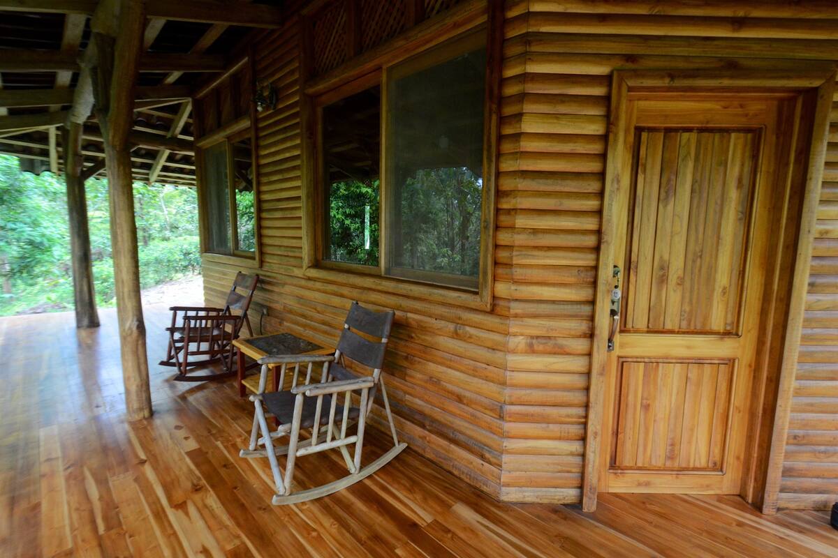 A wooden cabin with a porch, rocking chairs, and a door.
