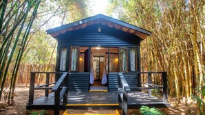 A wooden cabin with a porch, surrounded by bamboo forest. - Octagon Lodge (Karatu)
