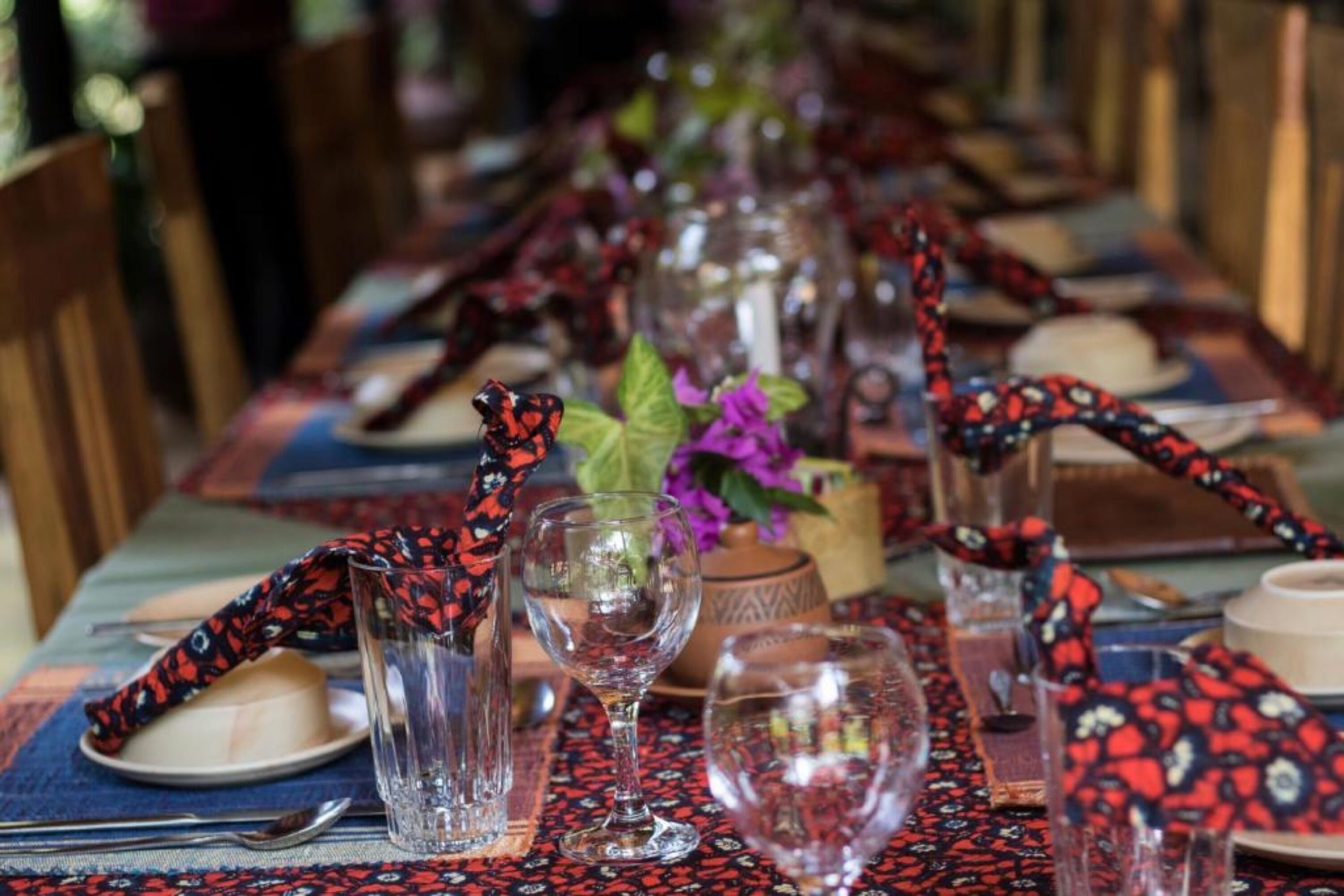 Una larga mesa de comedor dispuesta con copas, platos y un mantel decorado.
