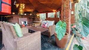 A covered outdoor seating area with wicker furniture, a brick wall, and potted plants. - Octagon Lodge (Karatu)