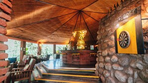 A rustic bar area with a dartboard, wooden furniture, and a stone wall. - Octagon Lodge (Karatu)
