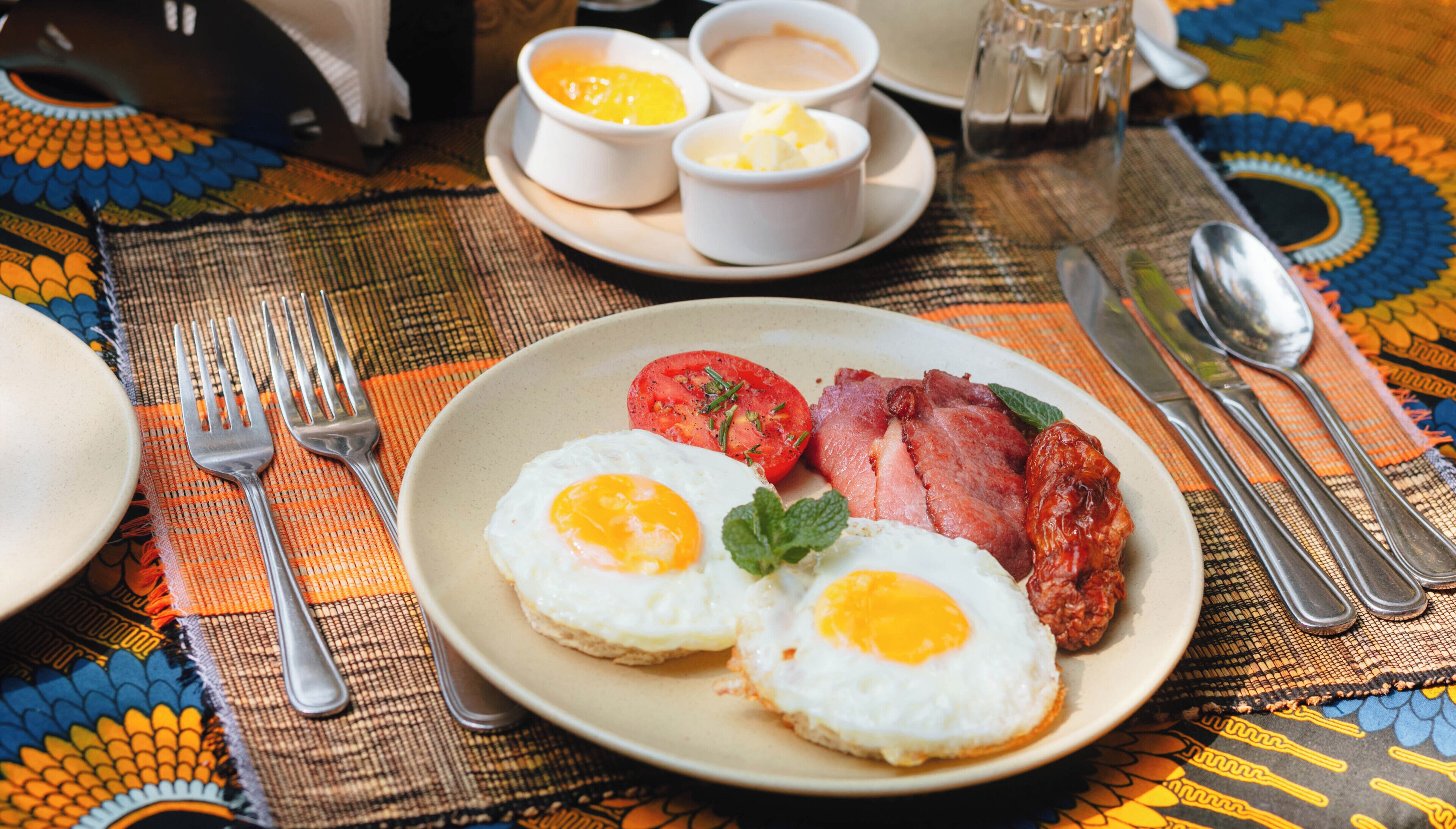 Un plato de desayuno con huevos, tocino y tomates sobre un mantel estampado.