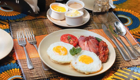 Un plato de desayuno con huevos, tocino y tomates sobre un mantel estampado.