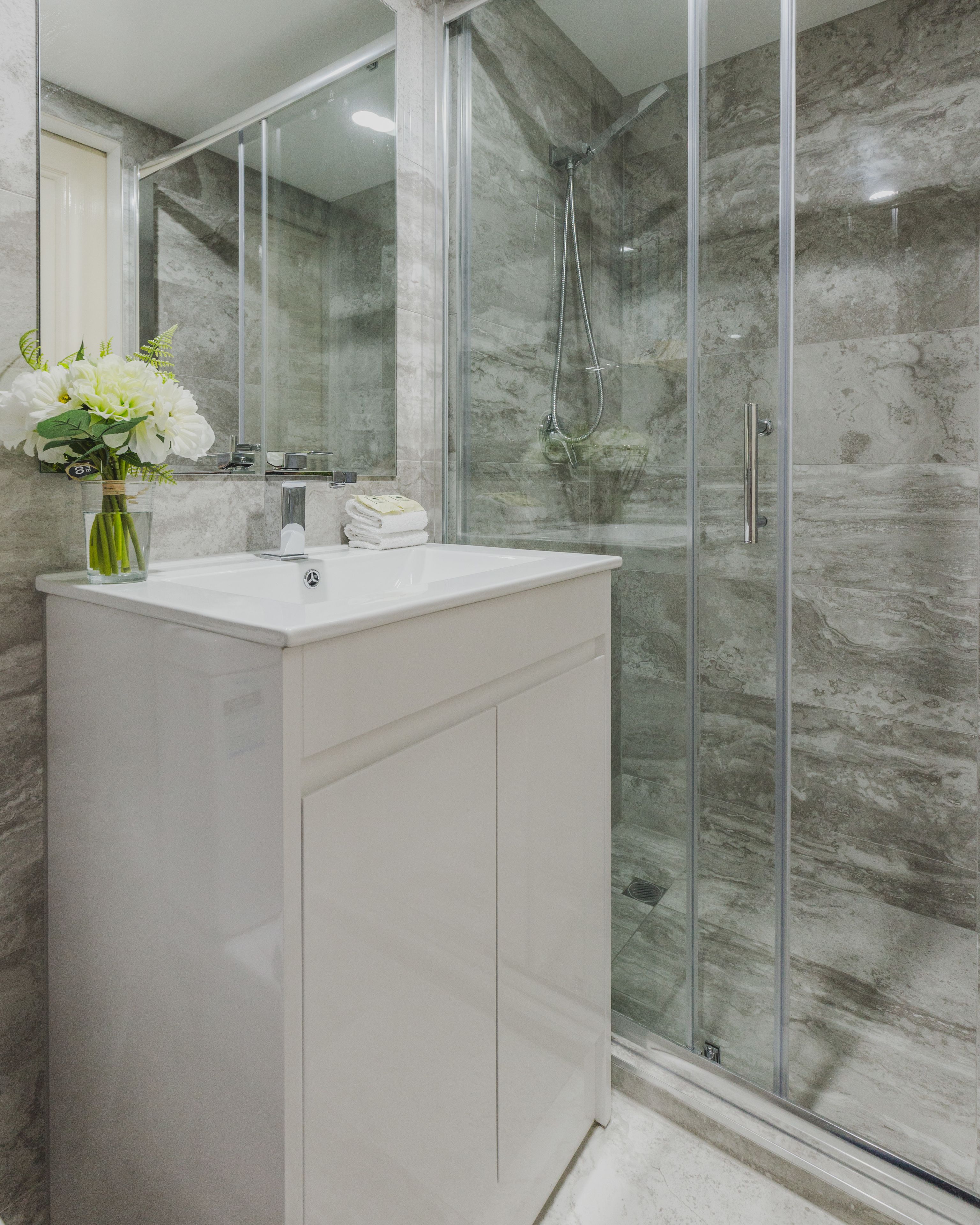 Une salle de bain moderne avec une douche à parois de verre, un meuble-lavabo blanc et un vase rempli de fleurs blanches.