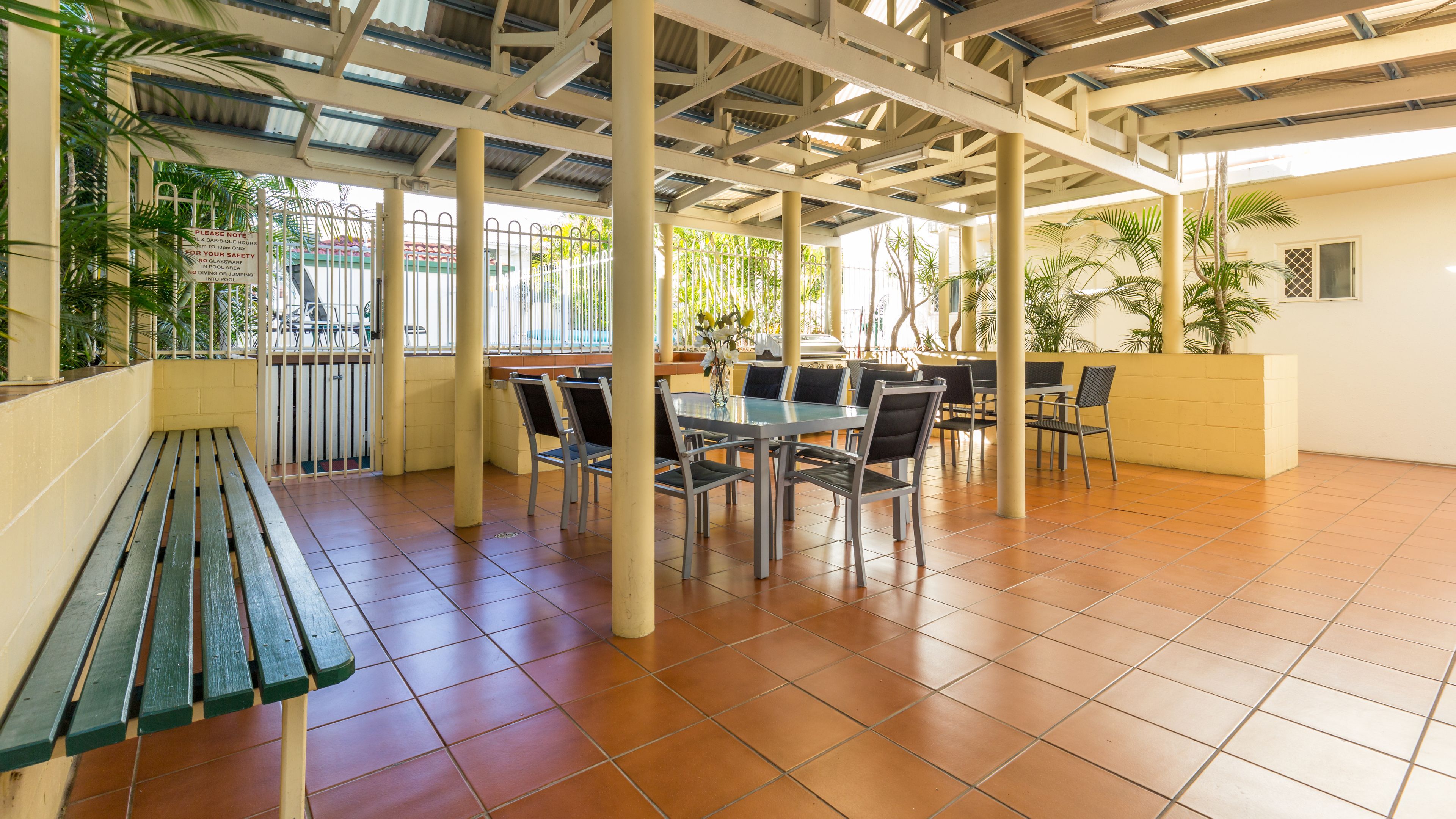 Een terras buiten met een overdekte zithoek, betegelde vloer en potplanten.