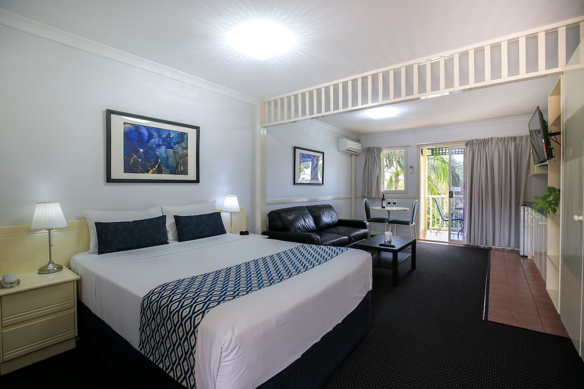 A hotel room with a bed, a desk, a chair, a sofa, a TV, and a balcony with curtains.