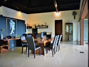 Un comedor moderno con una mesa y sillas de madera, una cocina al fondo y un cuadro grande en la pared.