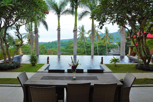 Un área de comedor al aire libre con vista a una piscina y palmeras.