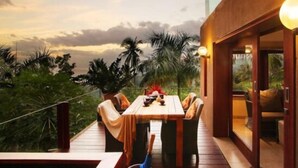 A wooden deck with a table and chairs, overlooking a tropical landscape with palm trees and a sunset. - Villa Tiara Lombok Island (Senggigi)
